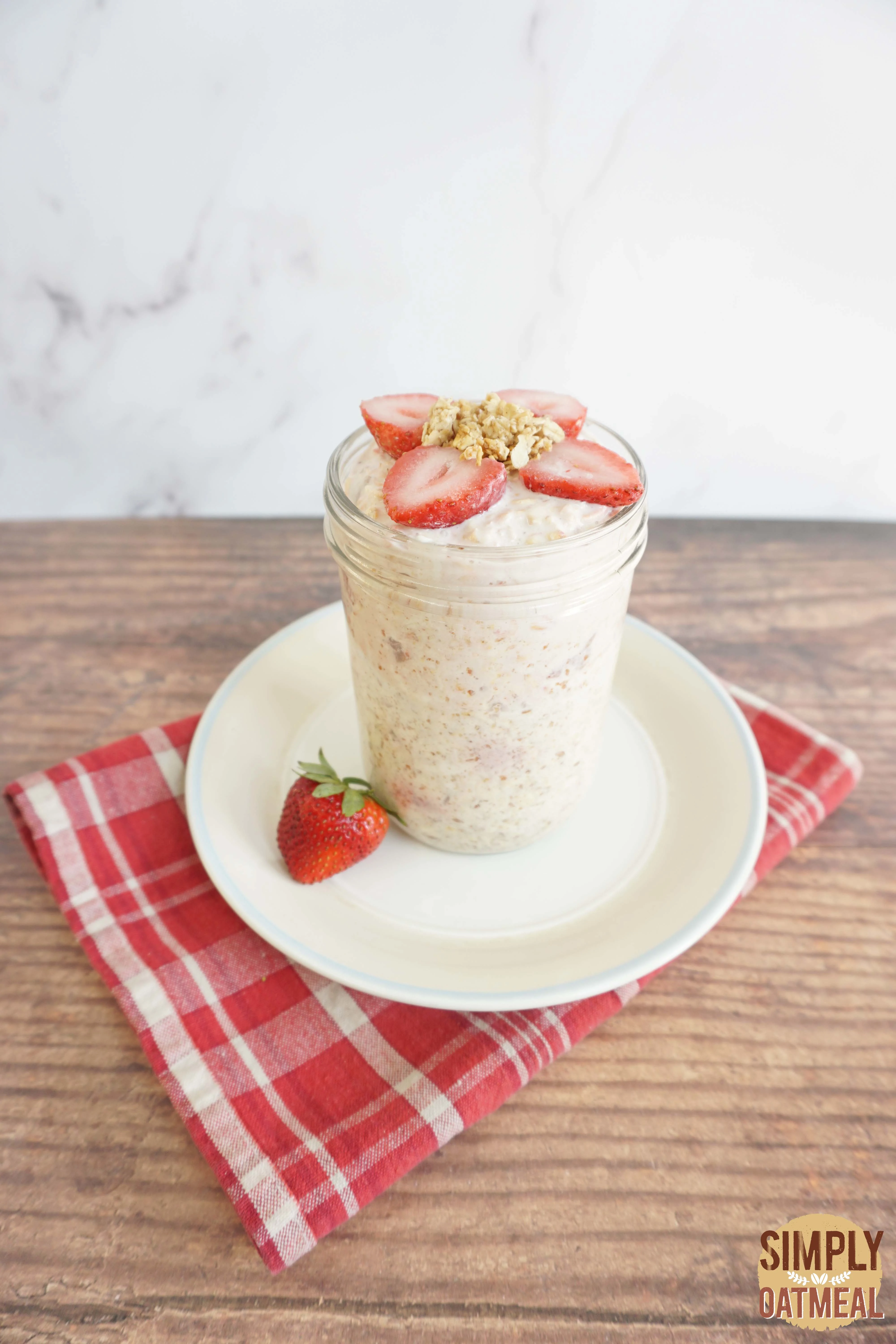 Strawberry yogurt overnight oats served in a mason jar topped with honey baked granola and fresh strawberries