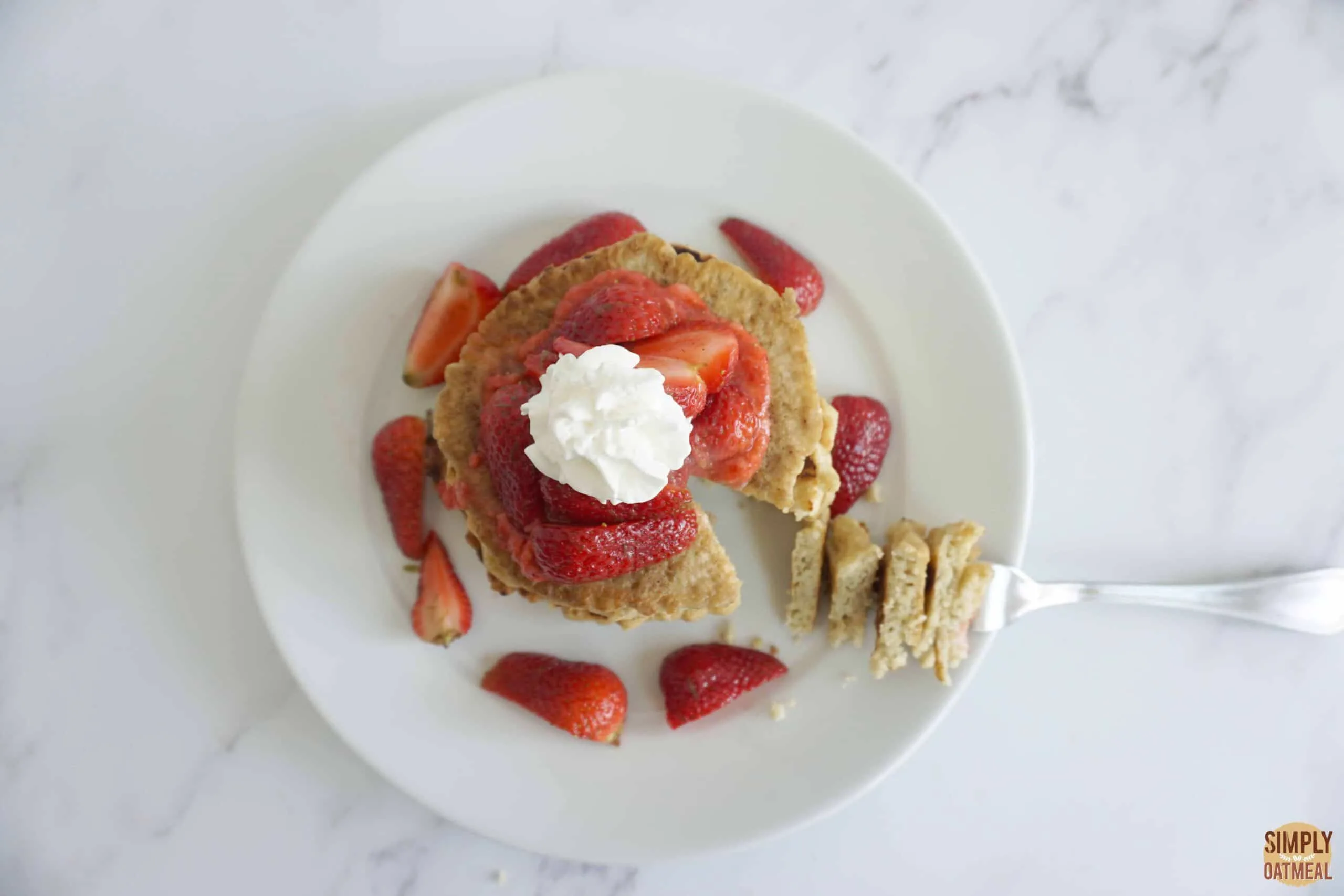 Coconut oatmeal pancakes topped with whipped coconut cream and strawberry lime syrup.
