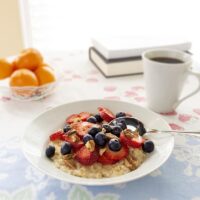 Steamy hot bowl of oatmeal topped with fresh berries and nuts. Hot coffee and fresh oranges on the side
