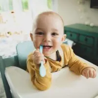 Side effects of oats for babies. Smiling baby in high chair eating oatmeal