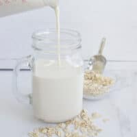 Pouring creamy oat milk without oil into a glass cup