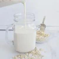 Pouring creamy oat milk without oil into a glass cup
