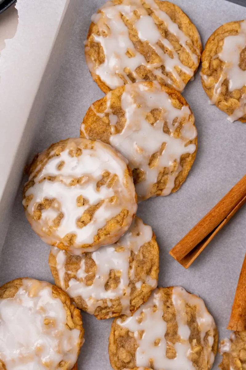 Glazed cinnamon cookies with white icing drizzle on parchment paper with cinnamon stick garnish.